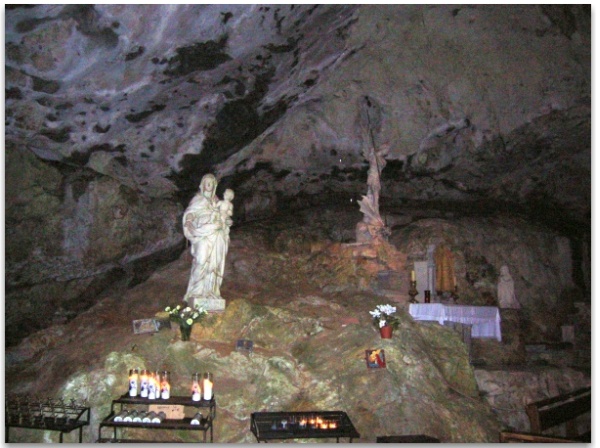 Votive candles lit before a statue of the Virgin and Child in the grotto